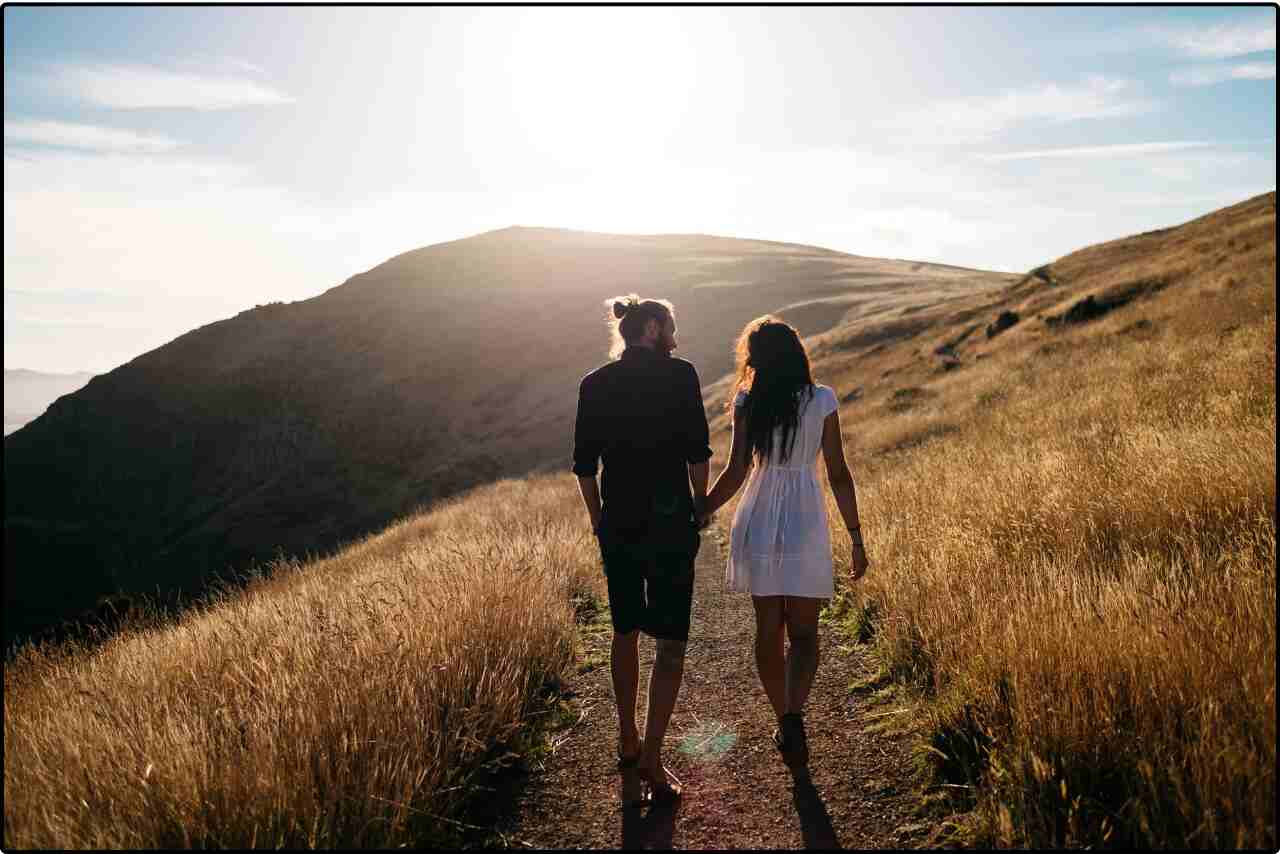 Peaceful scene of a couple walking on a path amidst high grassland, with rolling hills in the distance.